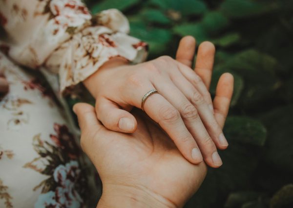 Close-up of a couple holding hands, highlighting a wedding ring in a garden setting.